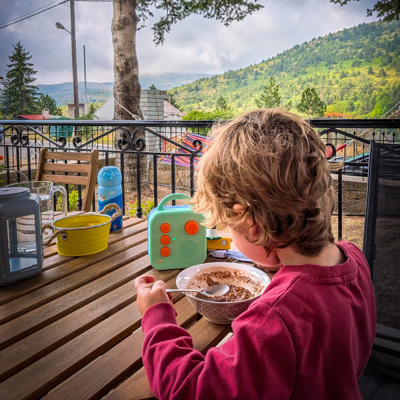 A toddler eating breakfast at a balcony table, with a Koobiba beside the bowl