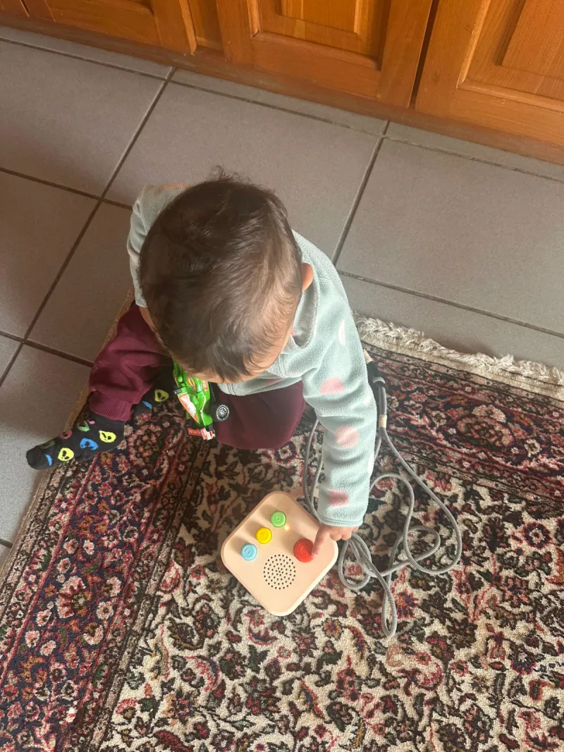 Toddler sitting on a rug, pressing colorful buttons on the Koobiba audio player